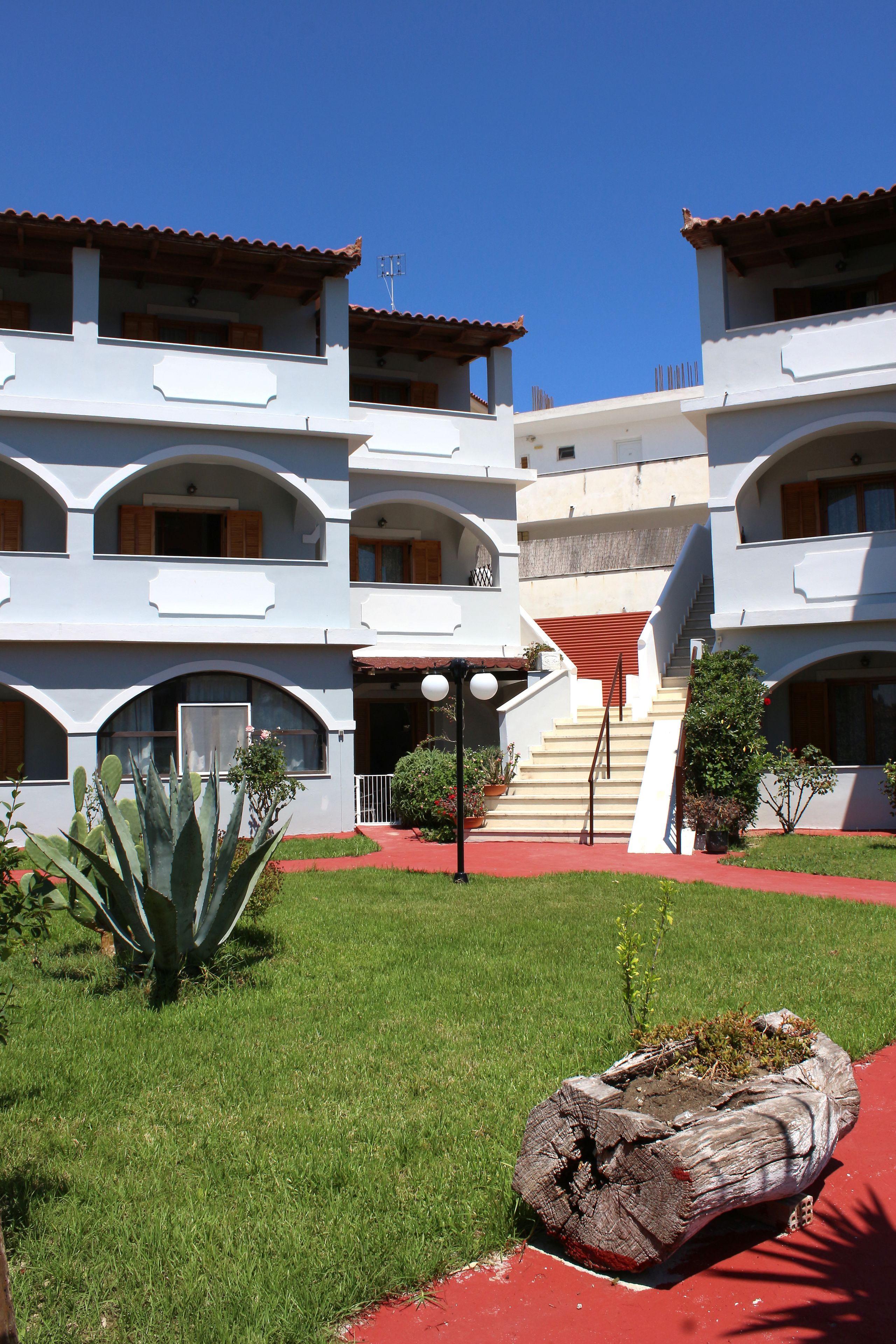 A multi-story building with a red-tiled roof, a central staircase, and a red pathway leading to the entrance.