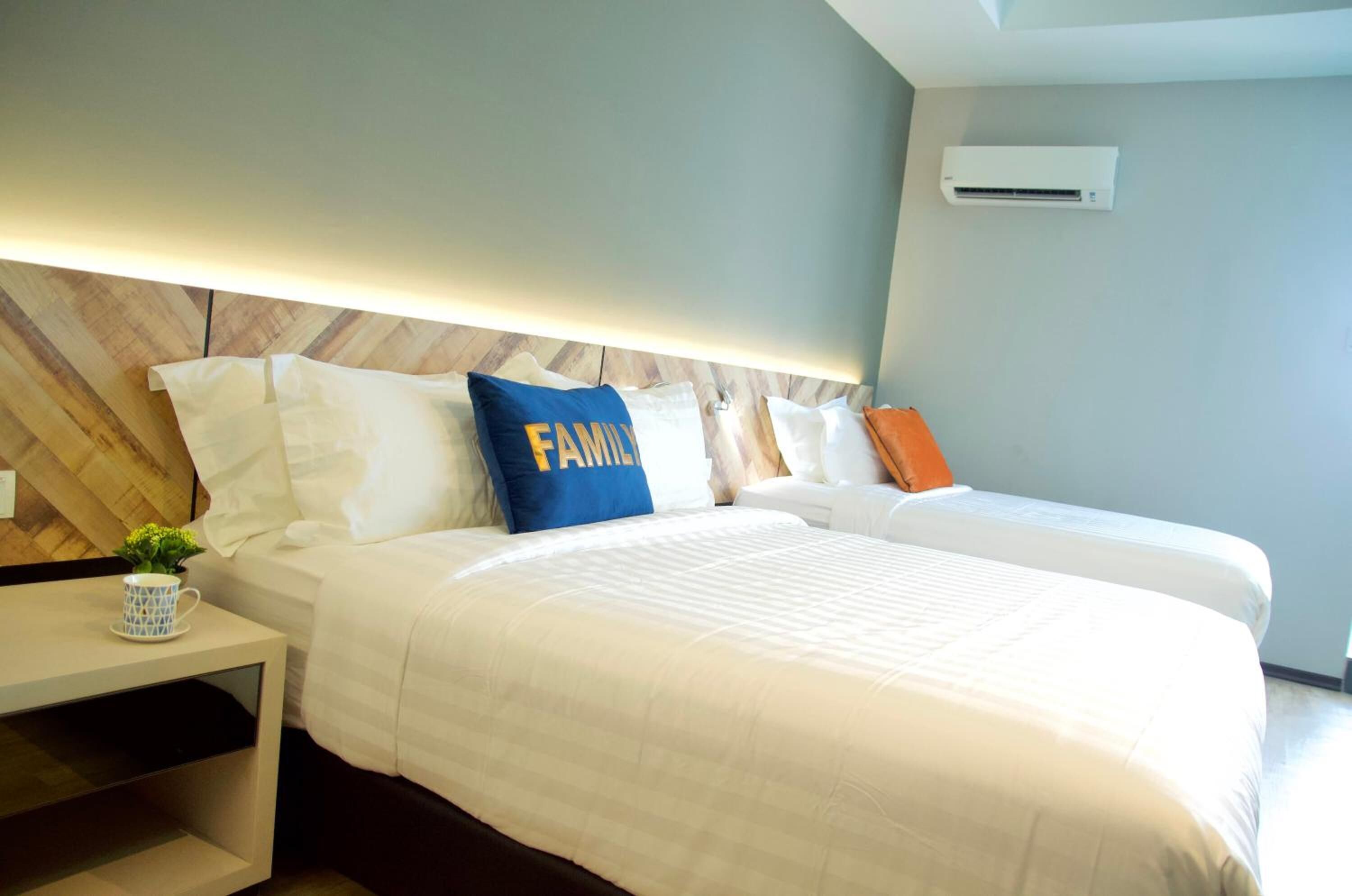 Ein Hotelzimmer mit zwei Betten, einem Holzkopfteil, weißer Bettwäsche und einem kleinen Tisch mit einer Pflanze.