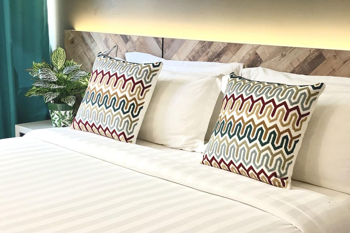 Ein Bett mit gemusterten Kissen, einer Topfpflanze und einem Holzkopfteil.
