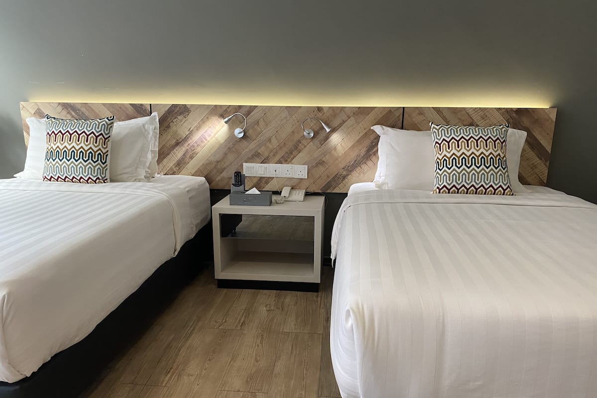 Ein Hotelzimmer mit zwei Betten, einem Nachttisch mit Lampe, Telefon und Fernbedienung.