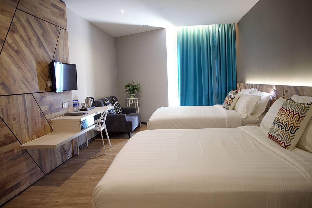 Ein modernes Hotelzimmer mit einem großen Bett, einem Schreibtisch mit Stuhl, einem Fernseher und einem Fenster mit blauen Vorhängen.