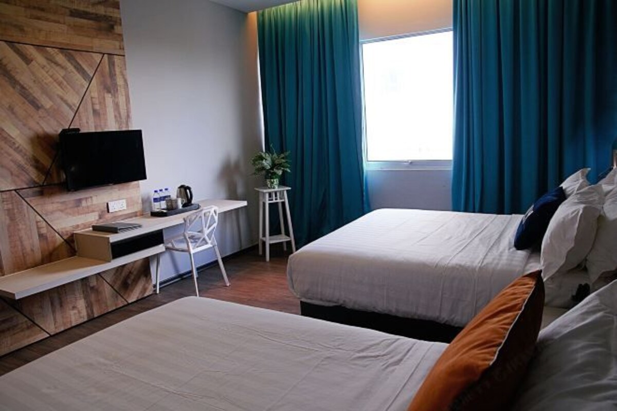 Een hotelkamer met twee bedden, een bureau met televisie, een klein tafeltje met een plant en een raam met gordijnen.