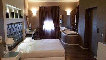 A hotel room with a large bed, a desk, a vanity with a mirror, and a bathroom with a sink and shower.