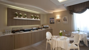 A modern dining area with a buffet setup, white chairs, and a ceiling light. - Hotel Morgana (Rodengo-Saiano)