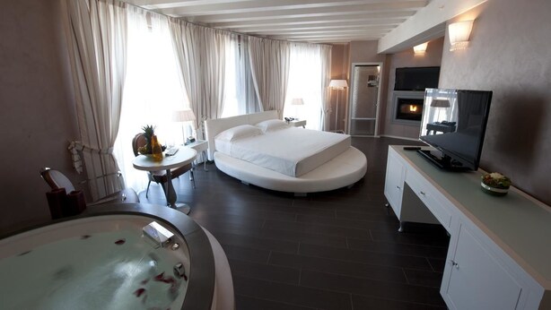 A modern hotel room with a large bed, a TV, a fireplace, a bathroom with a bathtub, and a dining area. - Hotel Morgana (Rodengo-Saiano)