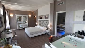 A modern hotel room with a large bed, a sitting area with a table and chairs, a glass-enclosed bathtub, and a fruit bowl on the side table.