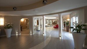 A spacious lobby with a curved ceiling, large white columns, and potted plants. - Hotel Morgana (Rodengo-Saiano)