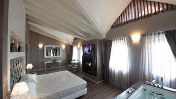 Une chambre d’hôtel moderne dotée d’un grand lit, d’un coin salon avec une cheminée, d’une télévision et d’une baignoire remplie de pétales de roses.