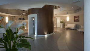 A modern lobby with a curved reception desk, a staircase, and a seating area with a white sofa and a small table. - Hotel Morgana (Rodengo-Saiano)