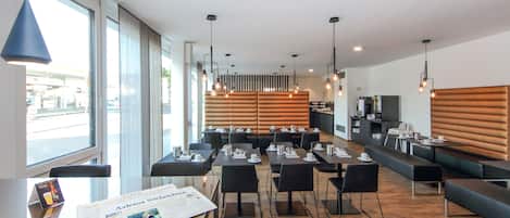 Un restaurante moderno con suelo de madera, mesas negras y una zona de estar con bancos.