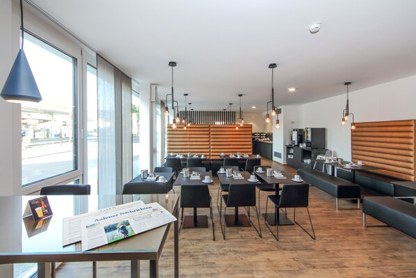 A modern restaurant with a wooden floor, black tables, and a seating area with benches. - Design & Lifestyle Hotel Estilo (Aalen)