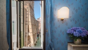 A room with a view of a narrow street through an open window, a wall-mounted light fixture, and a vase with flowers. - Ca' Lavezzera (Venice)