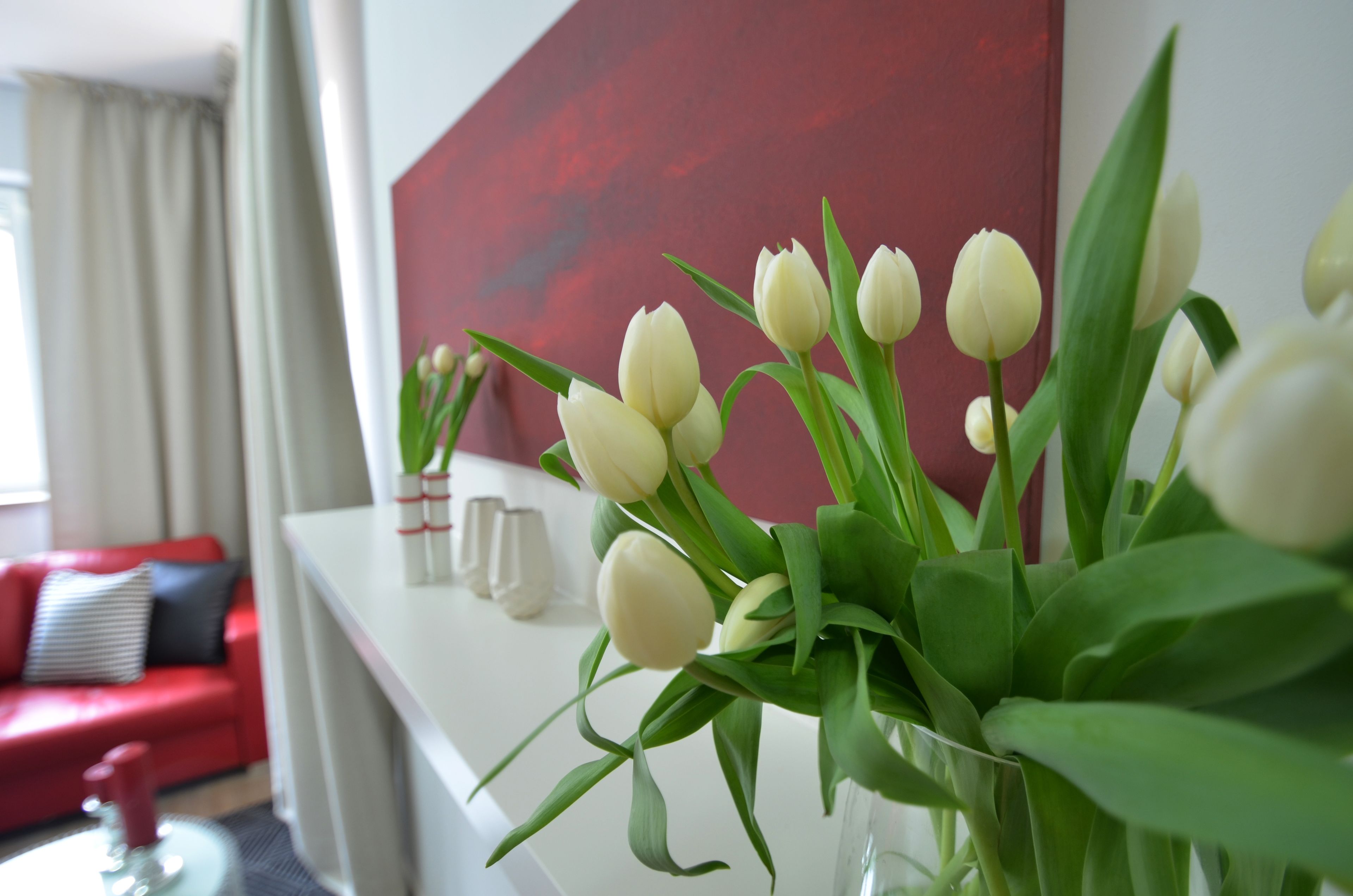 A living room with a red couch, a white coffee table, and a vase with white tulips.