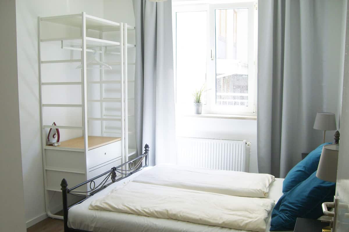 Un dormitorio con cama, armario, ventana con cortinas y radiador.