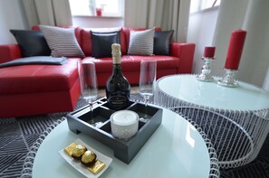 A modern living room with a red sofa, a white round table, and a bottle of champagne.