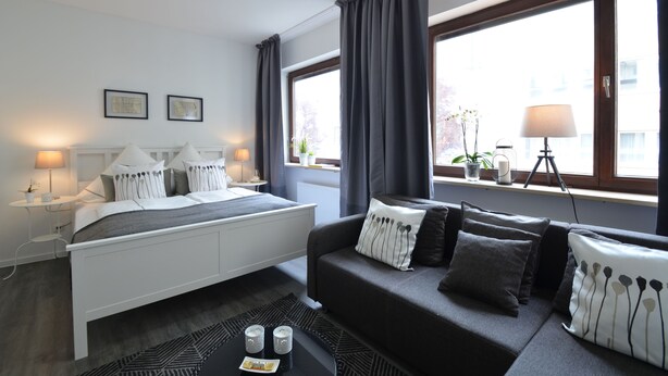 Un dormitorio moderno con cama, sofá y ventana con cortinas.