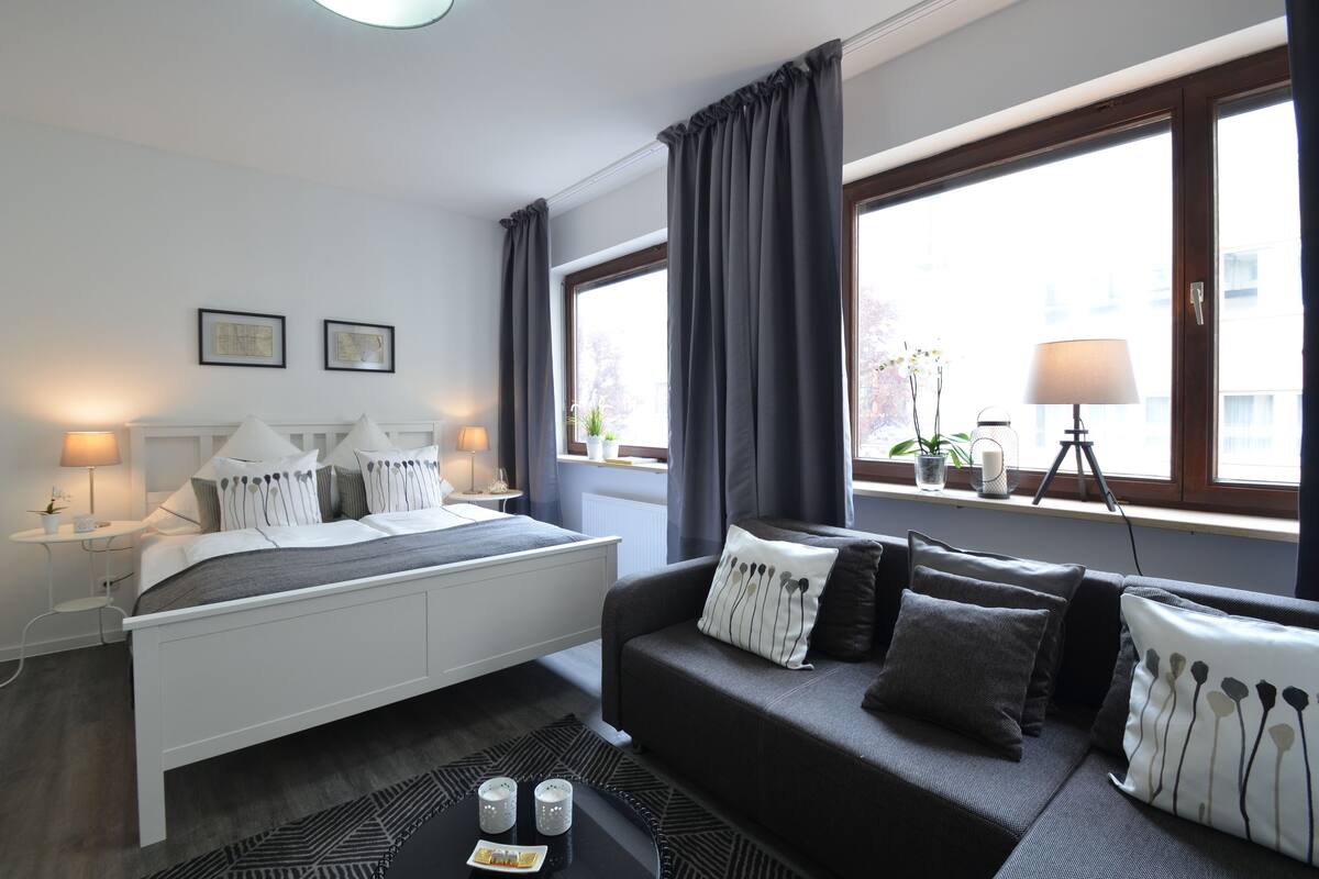 Un dormitorio moderno con cama, sofá y ventana con cortinas.