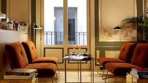 A room with two brown armchairs, a small table with a drink and a book, and a window with a view of the outside.