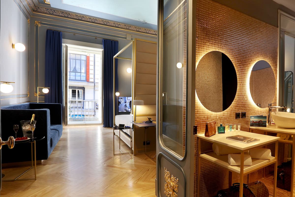 Un baño moderno con un espejo grande, un lavamanos y tocador. Hay una puerta que da a otra habitación.