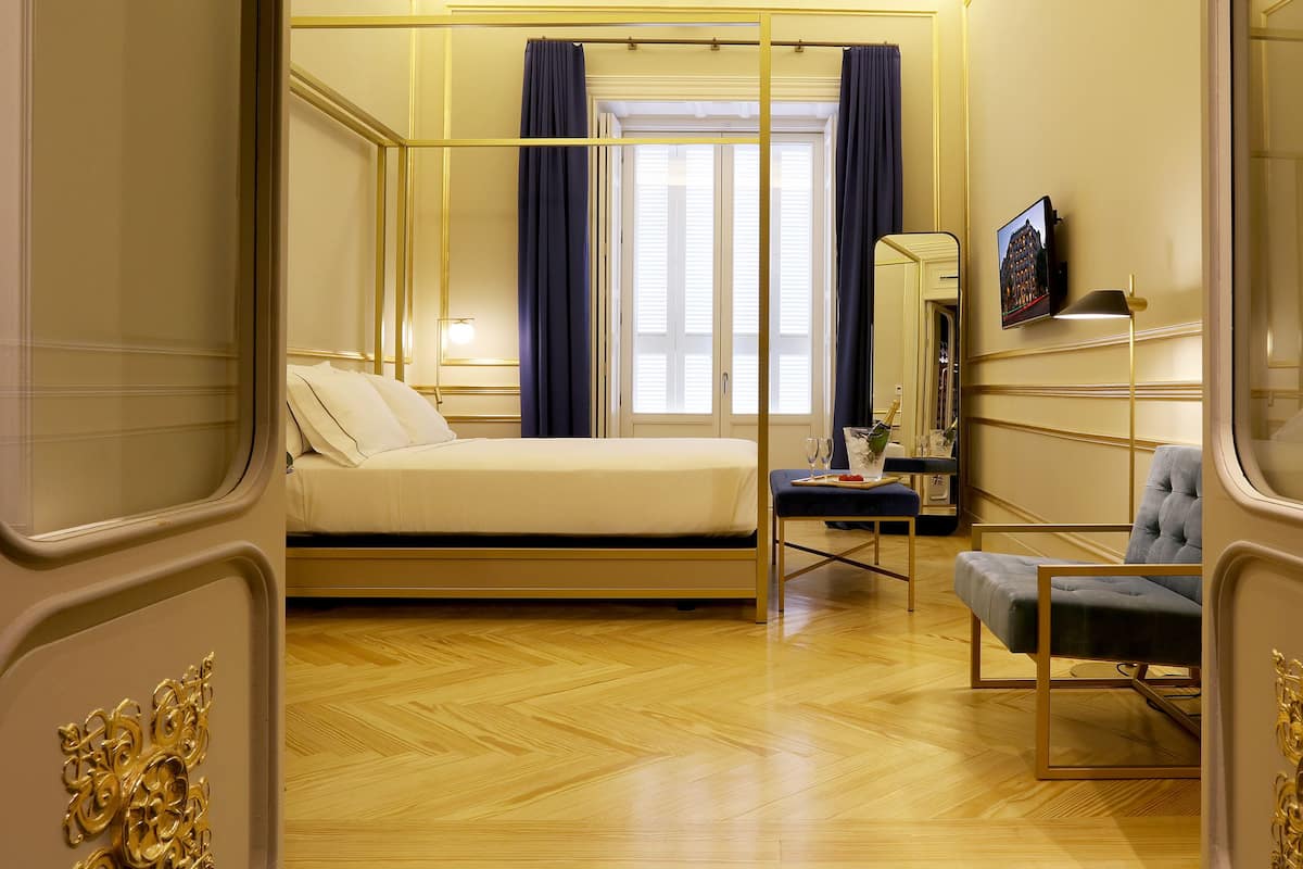 Un dormitorio con una cama, un escritorio con una silla, un espejo y una ventana con cortinas.