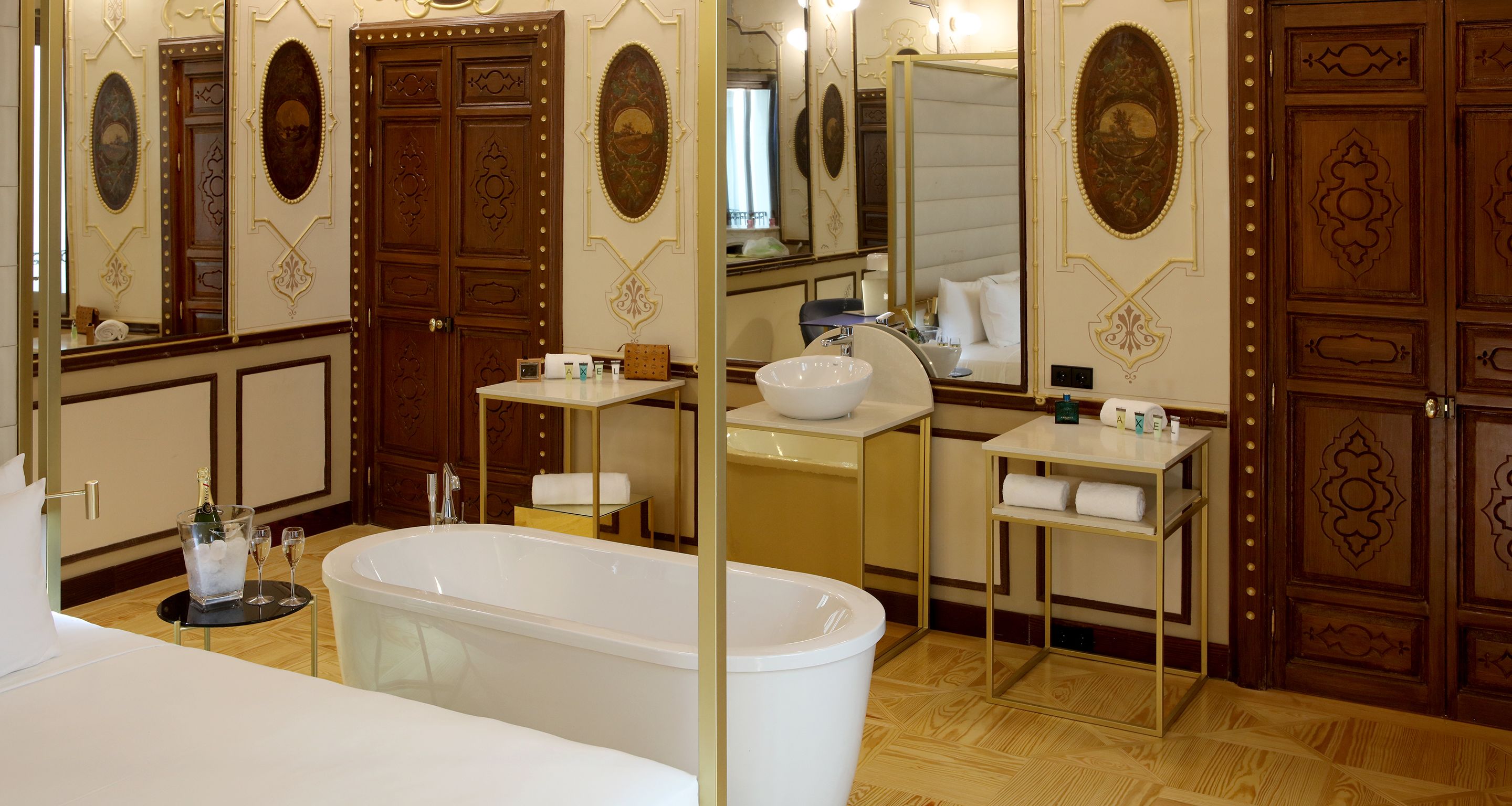 A luxurious bathroom with a large bathtub, a sink, and a mirror. There is a bottle of champagne and two glasses on a small table.