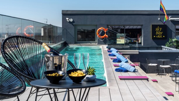 A modern outdoor pool area with lounge chairs, a bar, and a sign for 'Sky Bar by AXL'.