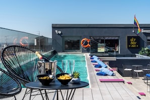 Un área de piscina moderna al aire libre con sillones de descanso, un bar y un letrero que dice 'Sky Bar by AXL'.