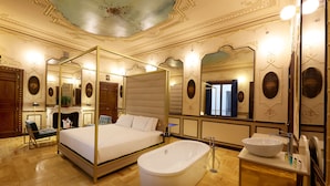 A luxurious bedroom with a four-poster bed, a large bathtub, and a vanity with a bowl sink.
