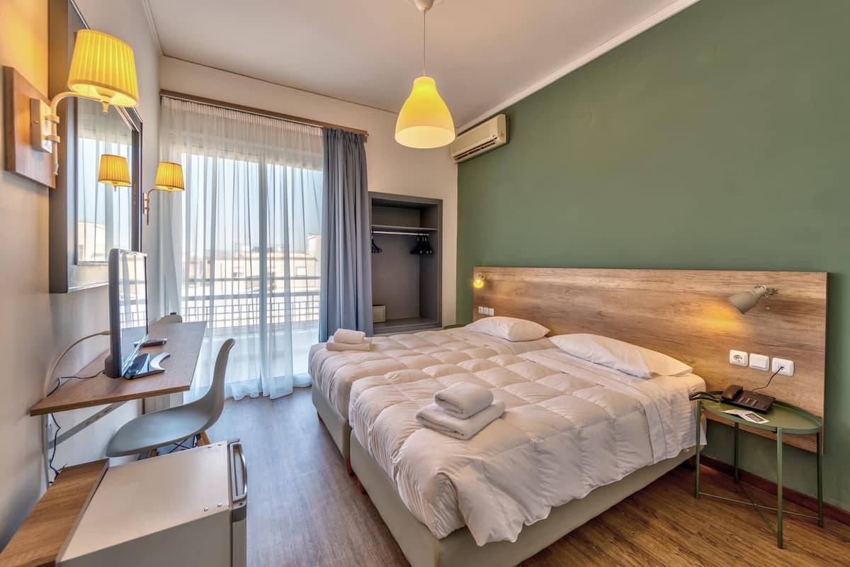 Habitación de hotel con cama, escritorio, silla y una mesita de noche con lámpara.