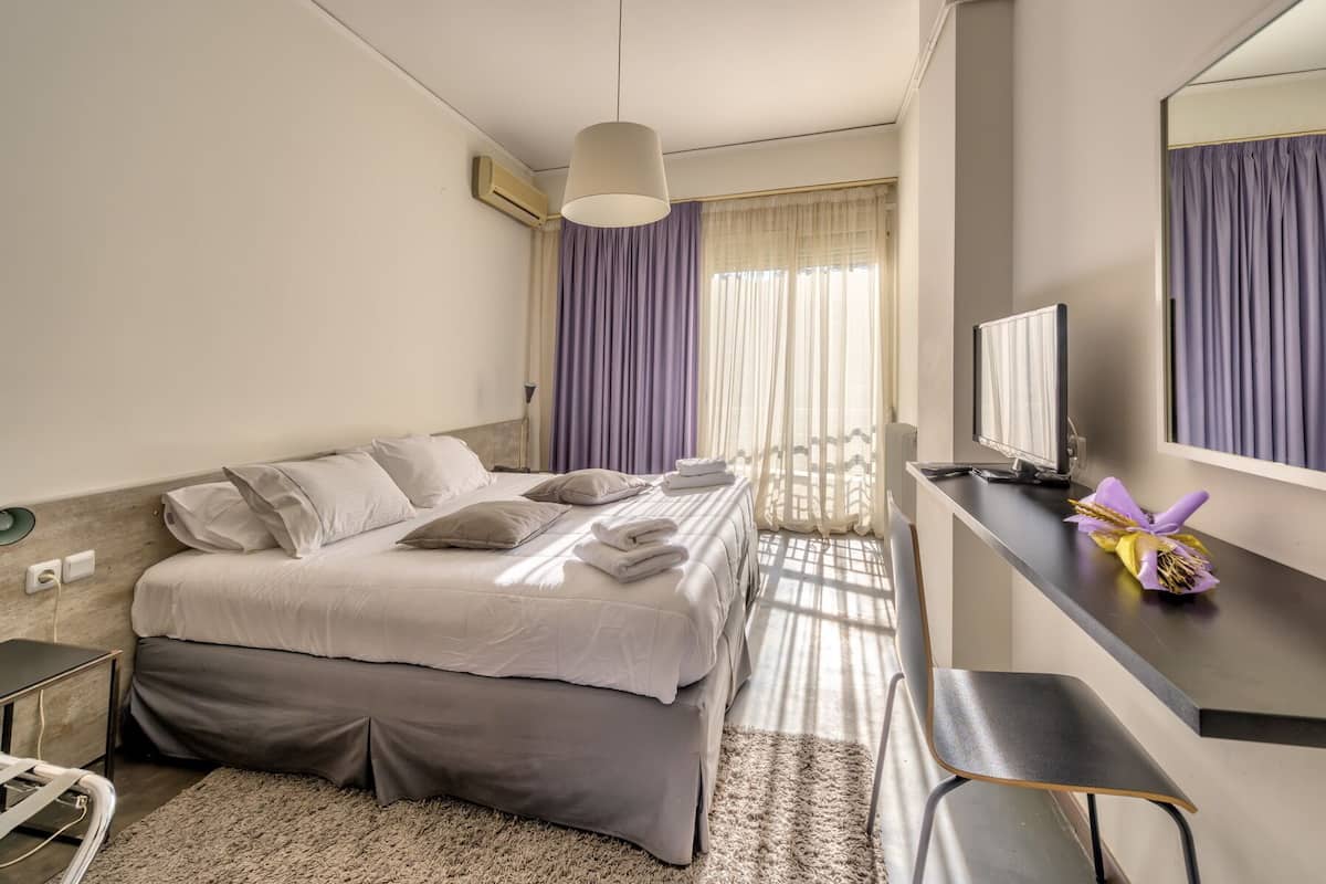 Una habitación de hotel con cama, mesita de noche, silla y escritorio con monitor de computadora.