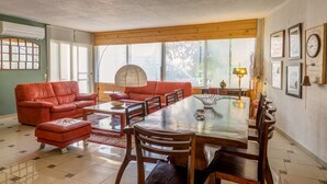 Un comedor con mesa y sillas de madera, un sofá rojo y un ventanal con luz natural.
