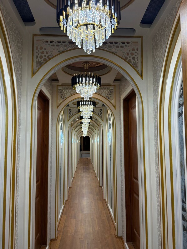 A grand hallway with ornate chandeliers, arched doorways, and patterned wall designs.