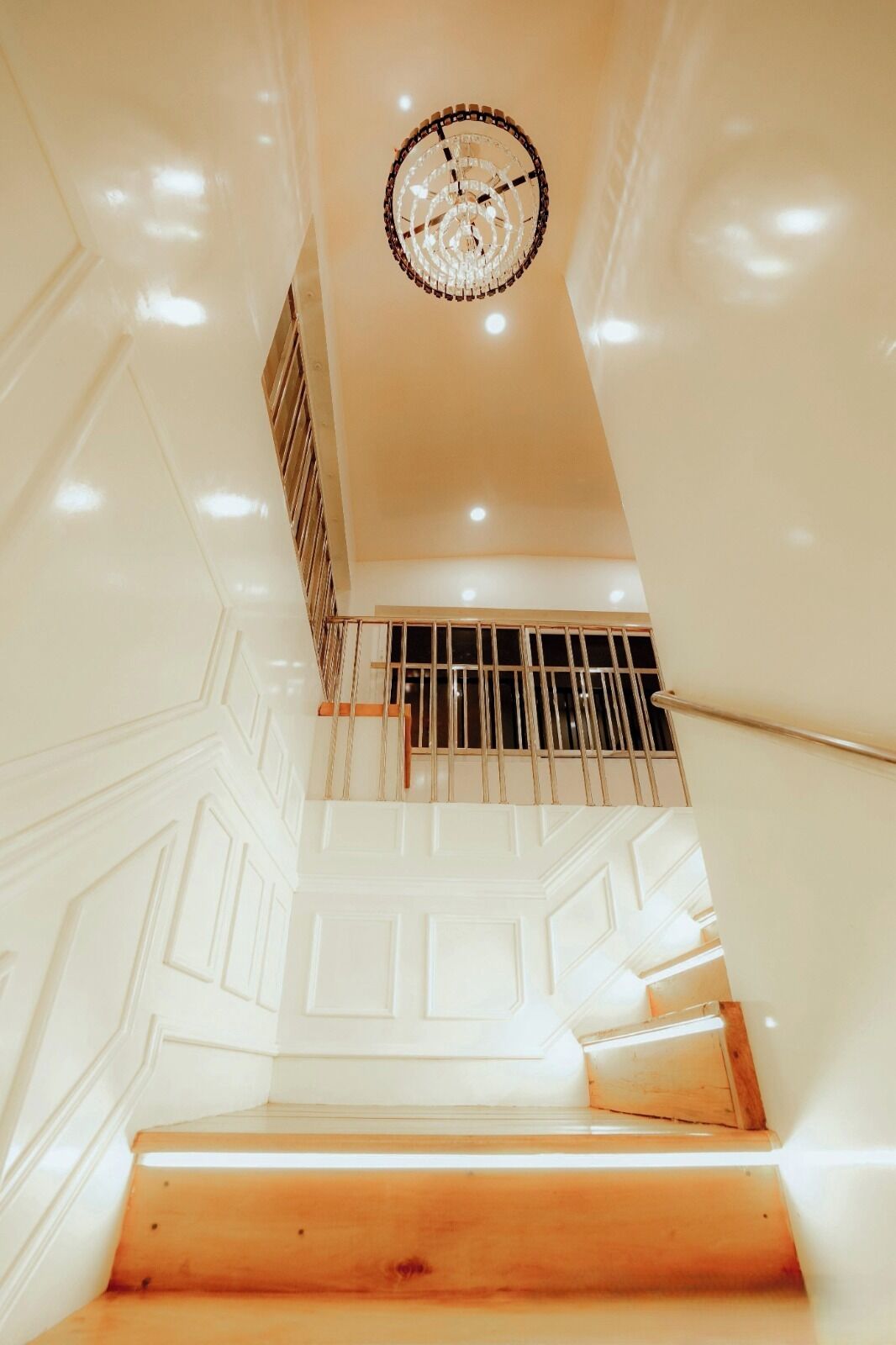 Una escalera con paredes blancas y barandilla de madera que conduce a una plataforma con baranda de metal.