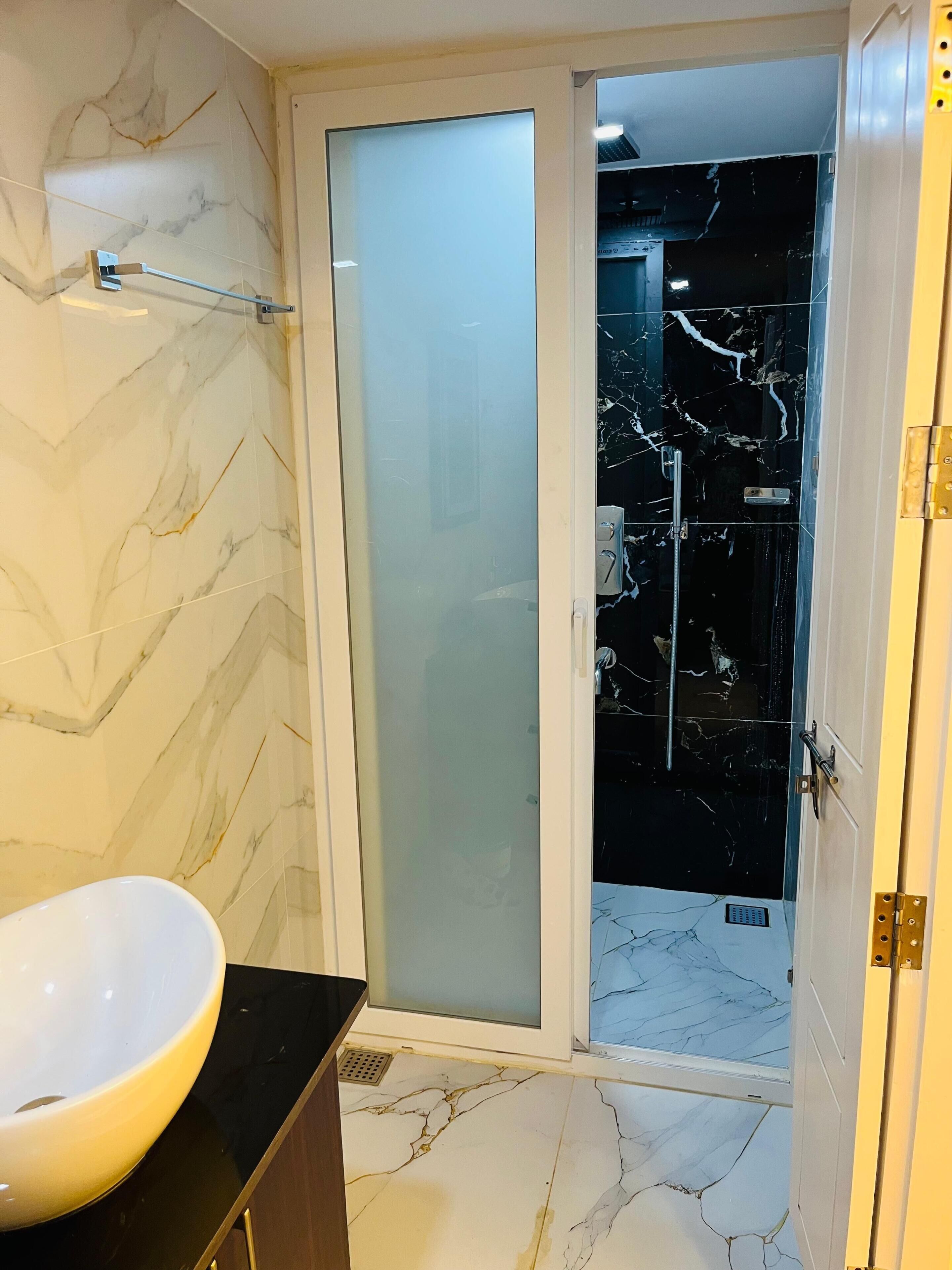 A bathroom with a marble wall, a glass shower enclosure, and a sink with a yellow basin.