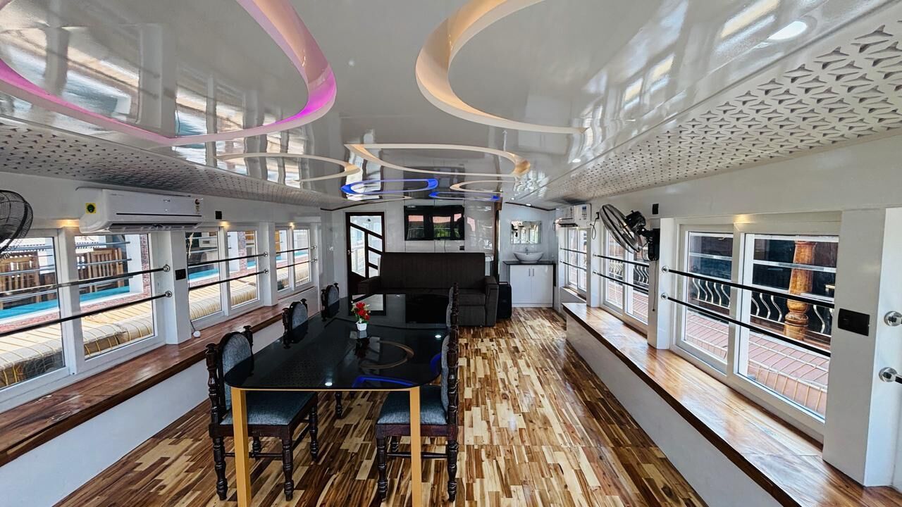 Un interior moderno con suelo de madera, una mesa central con sillas, un televisor y ventana con vista a una piscina.