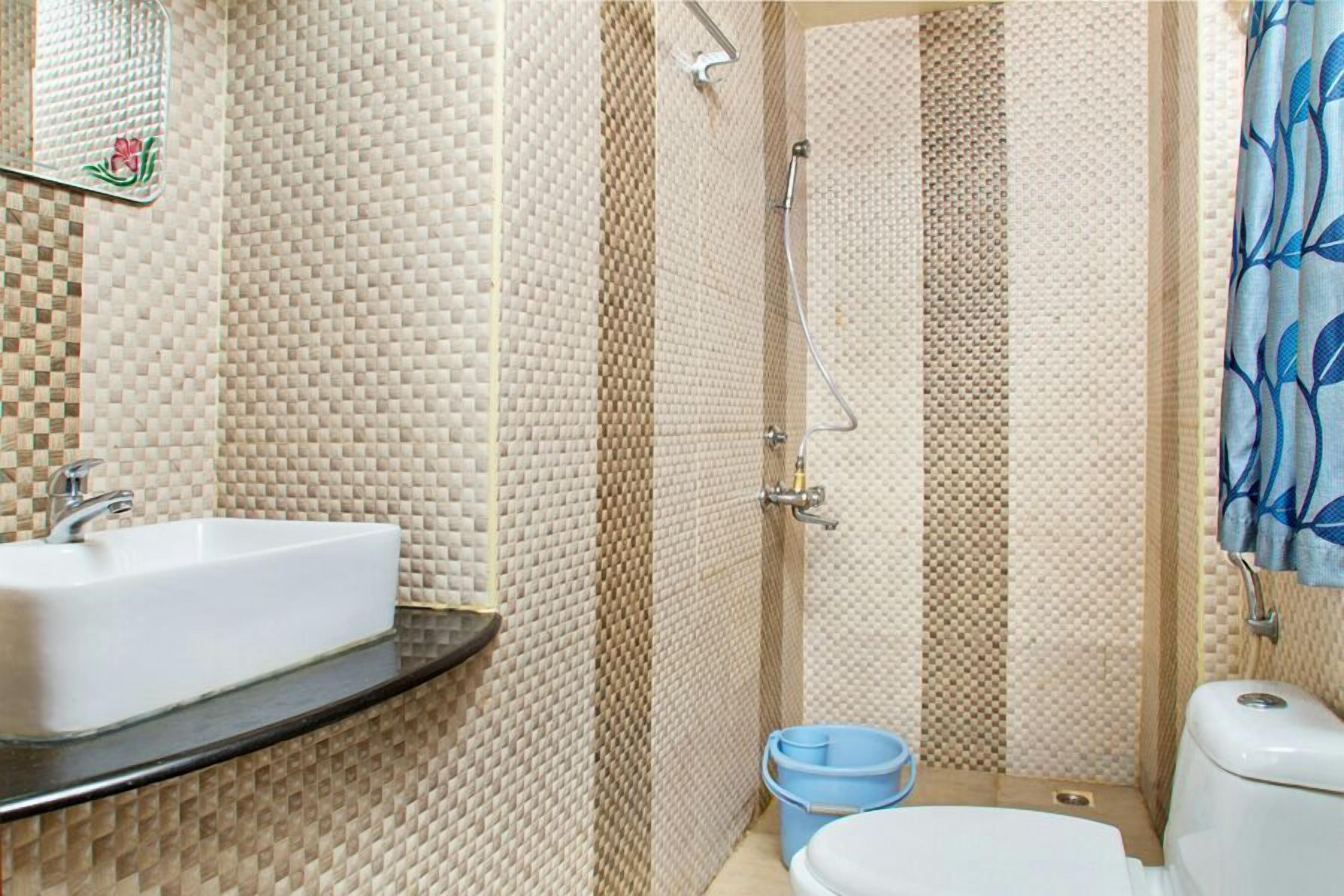 A bathroom with a tiled wall, a sink, a toilet, and a shower area.
