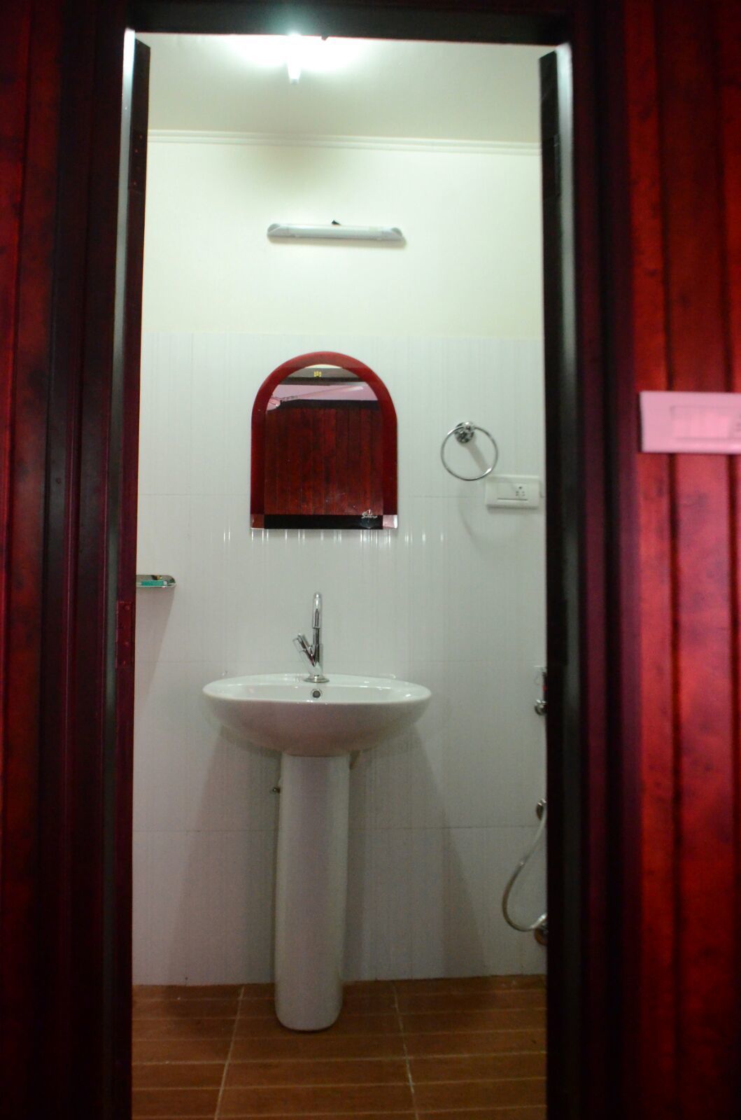 Une salle de bain avec un lavabo blanc, un miroir et une porte rouge.