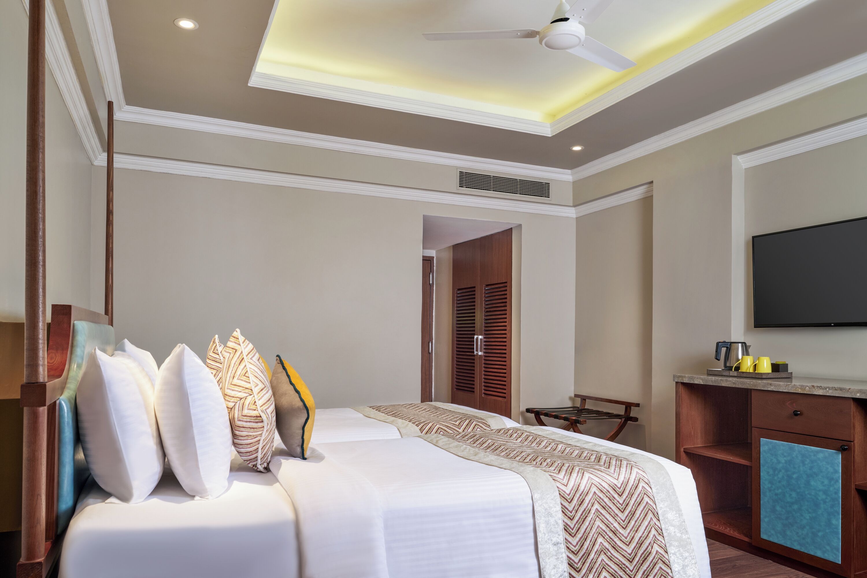 A hotel room with two beds, a ceiling fan, a TV, and a small kitchenette.