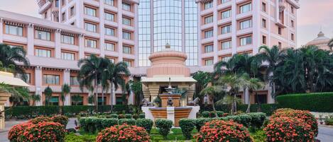A large hotel with a central fountain, surrounded by well-manicured gardens and palm trees.