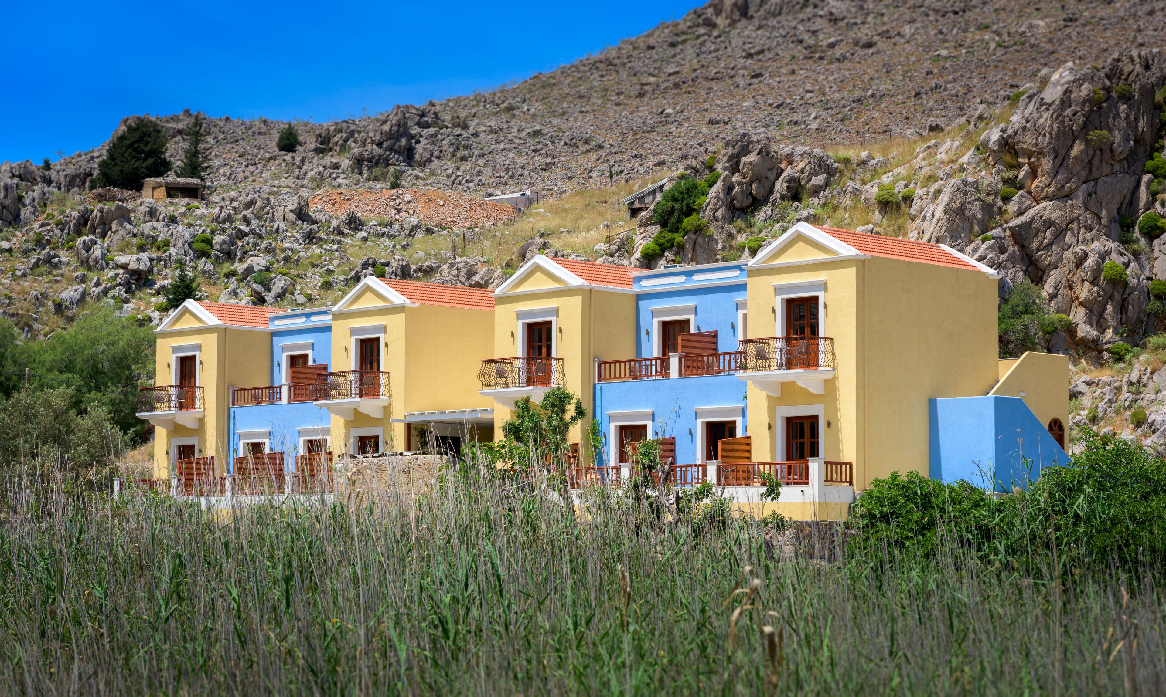 Una hilera de edificios de tres pisos con balcones, frente a una ladera rocosa.
