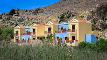 Una hilera de edificios de tres pisos con balcones, frente a una ladera rocosa.