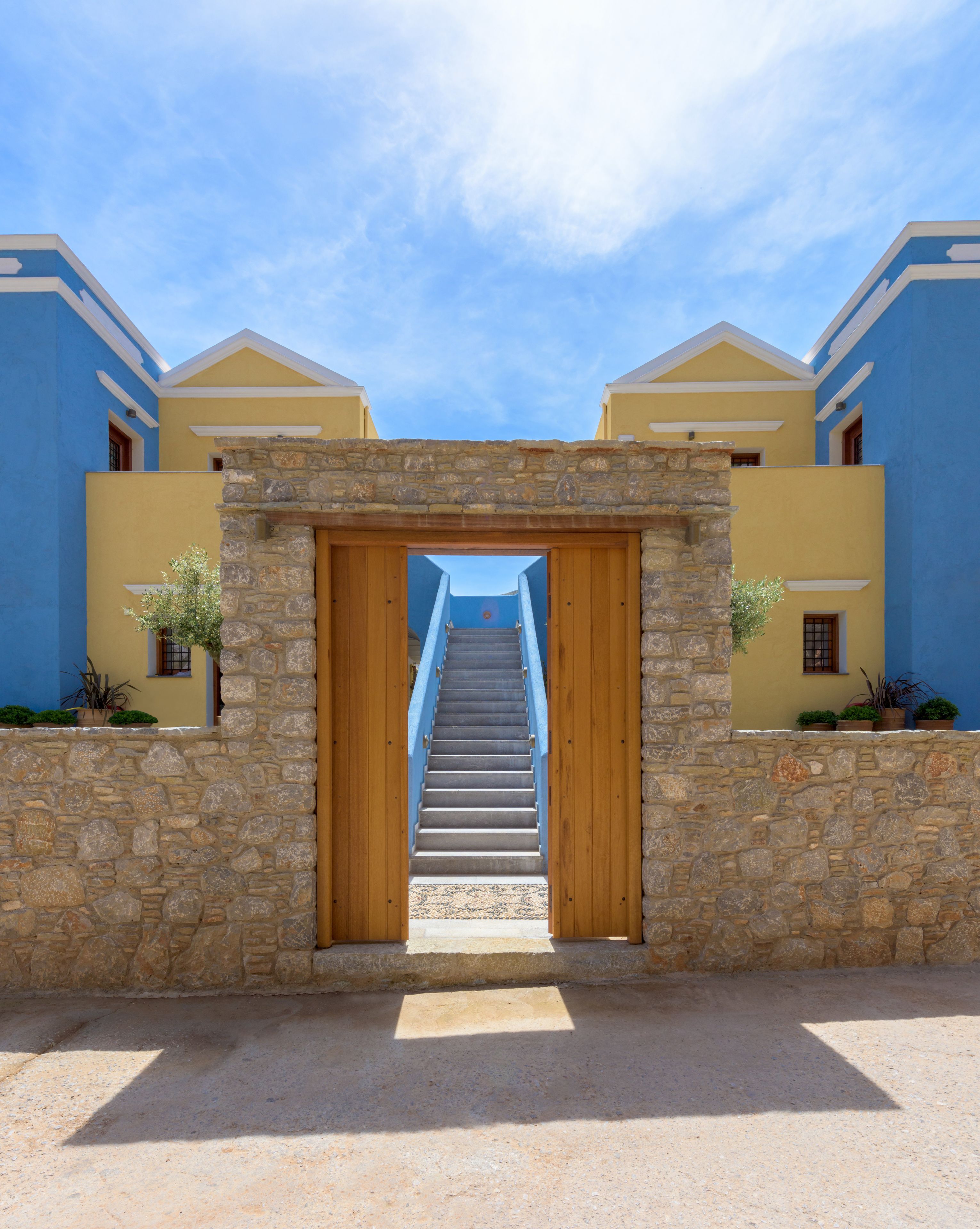 A stone staircase leading to a wooden door framed by a stone wall, flanked by two buildings with blue and yellow facades.