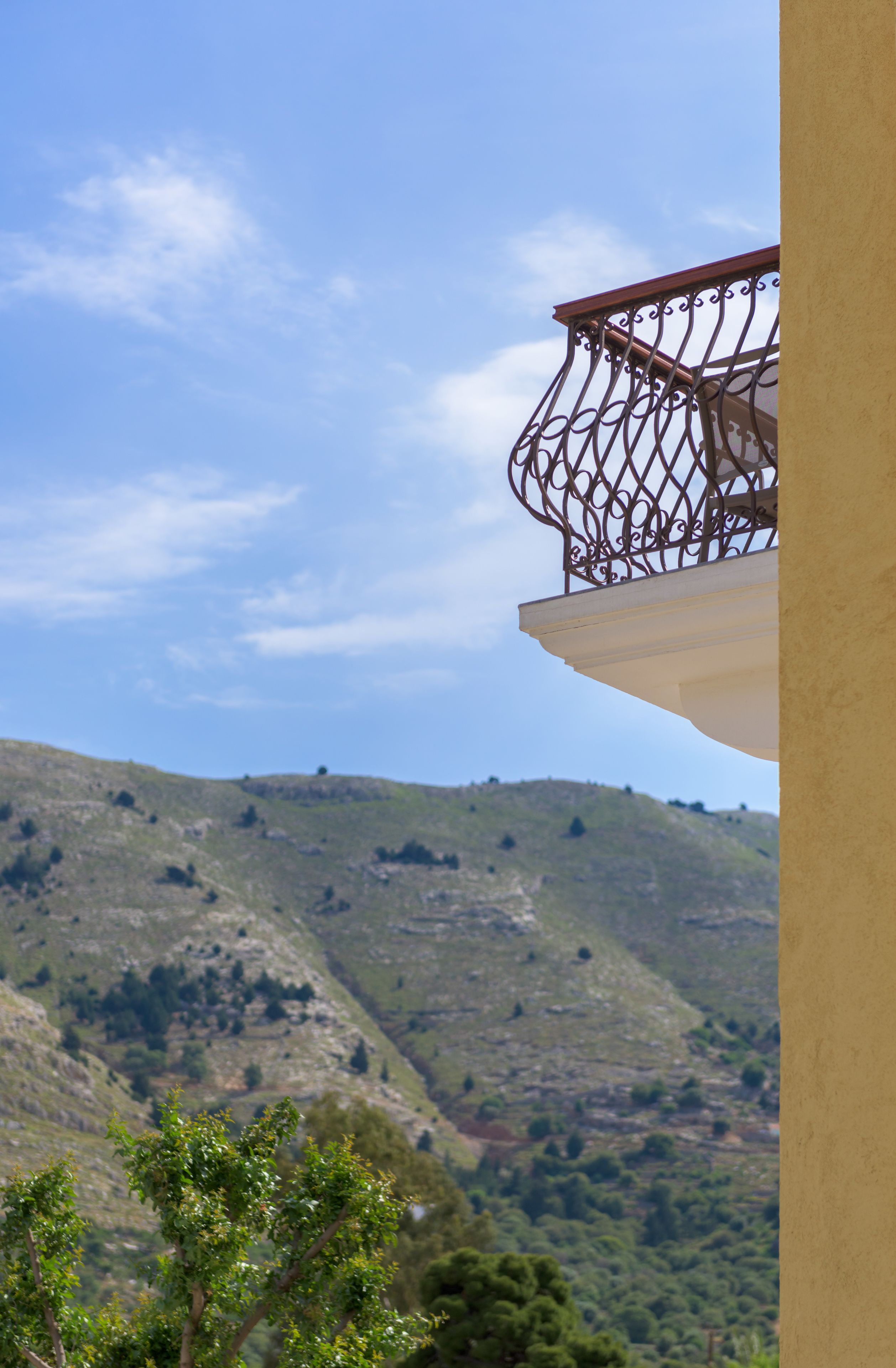 A balcony with a wrought iron railing overlooking a hilly landscape.