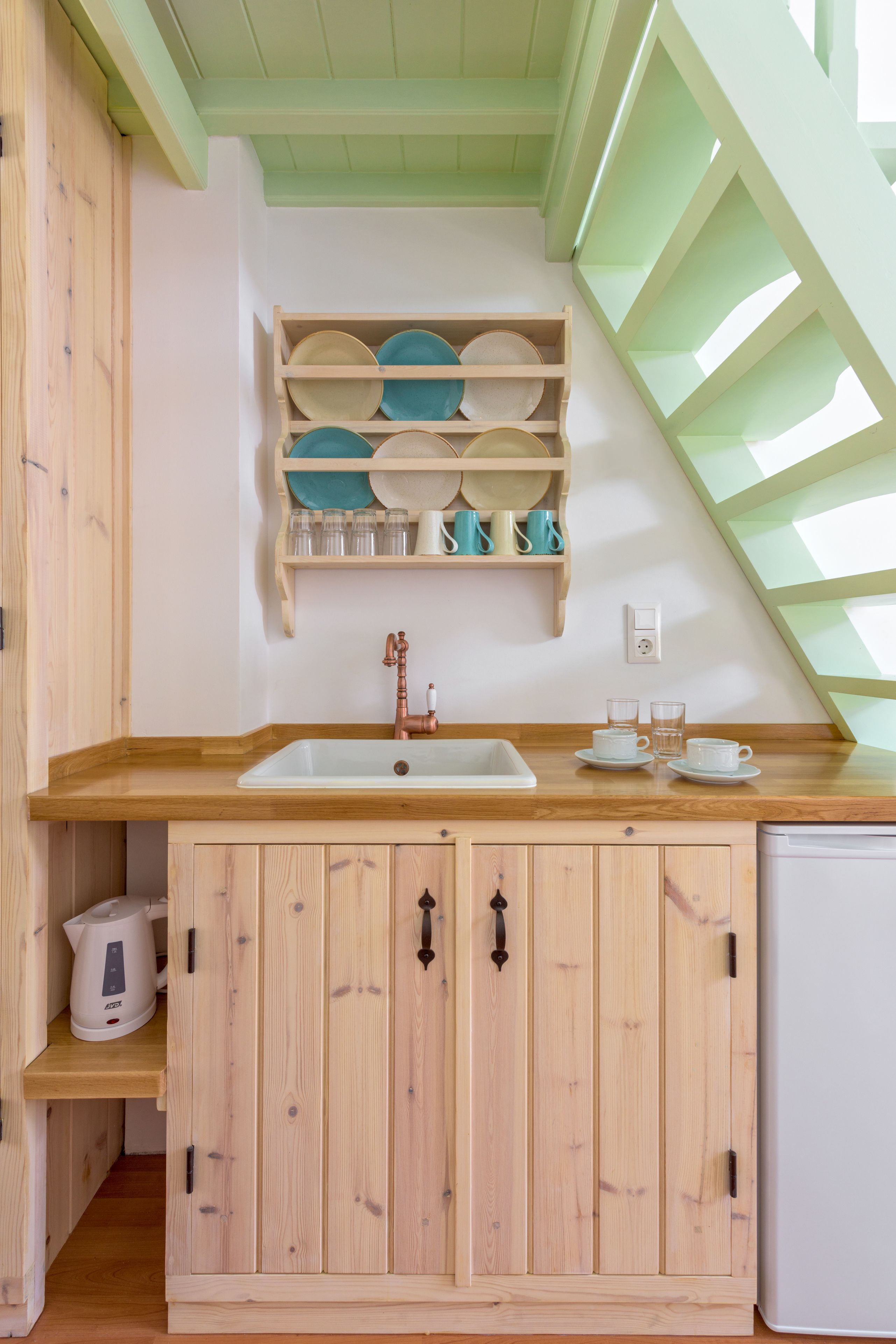 A kitchen with wooden cabinets, a white sink, and a countertop. There is a shelf above the sink holding plates and cups.