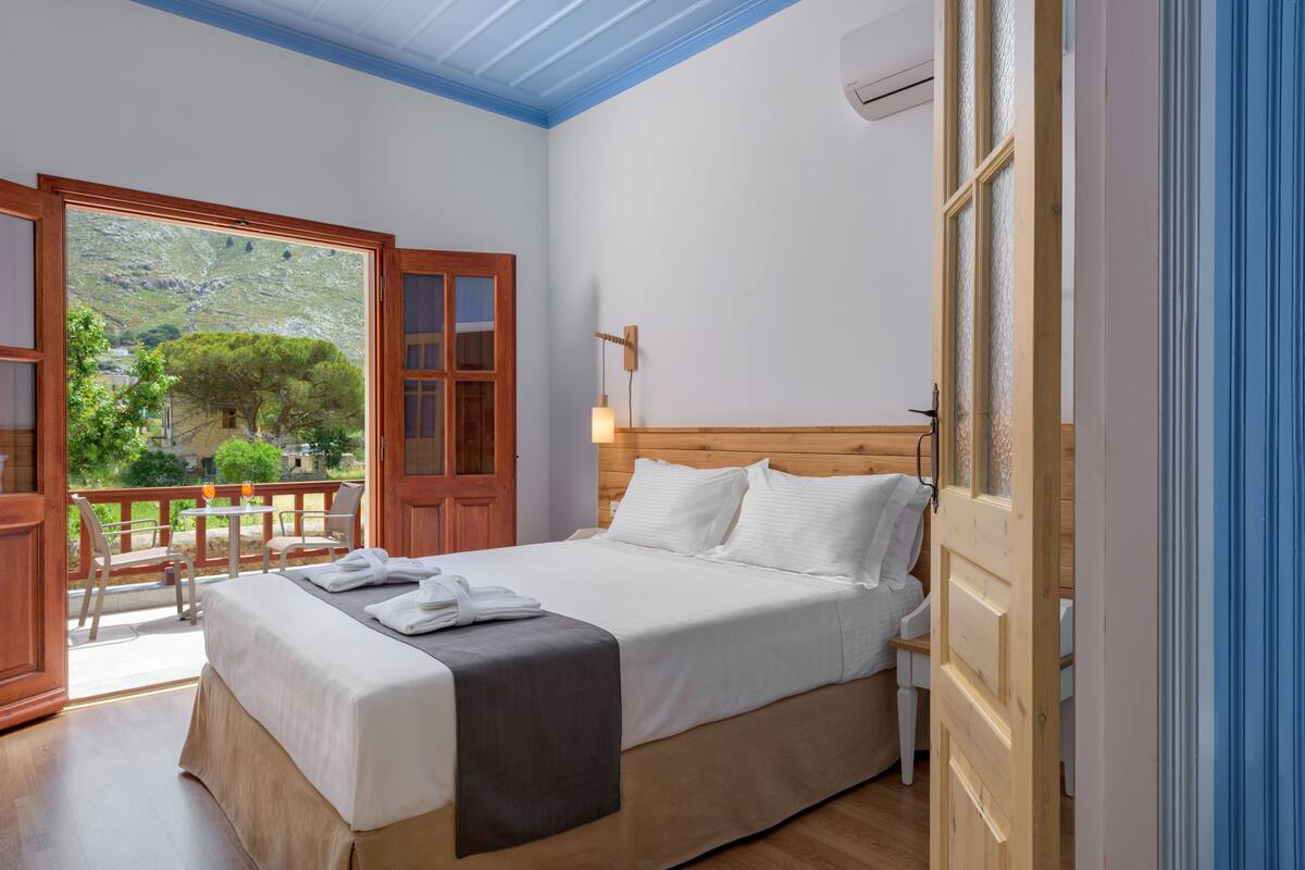 Un dormitorio con cama, cabecero de madera y vistas a un balcón con mobiliario exterior.