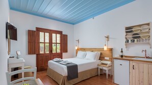 Un dormitorio con cama, mesitas de noche, escritorio y una pequeña kitchenette.