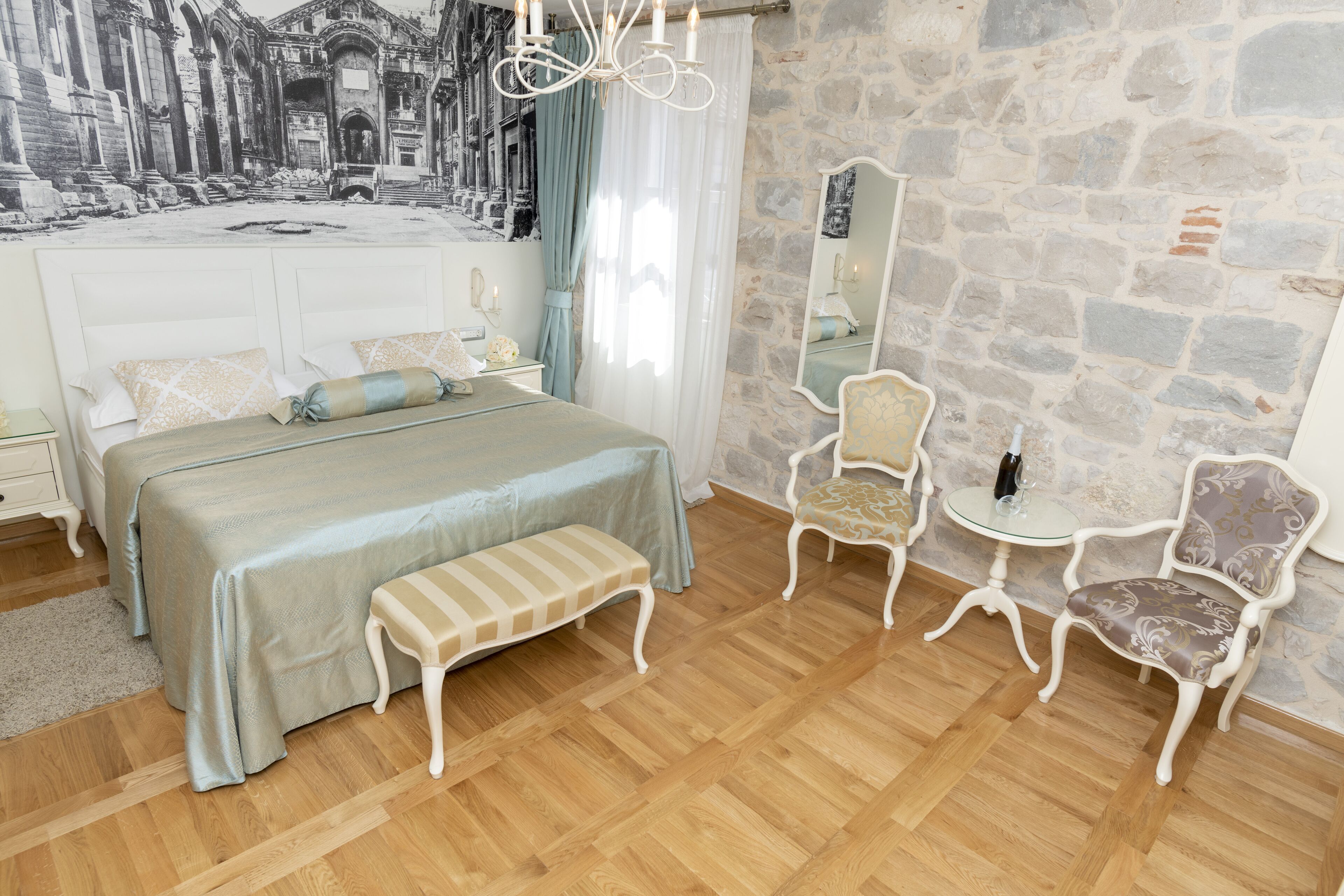 Ein Schlafzimmer mit einem großen Bett, einer Bank, zwei Stühlen, einem kleinen Tisch und einem Spiegel.