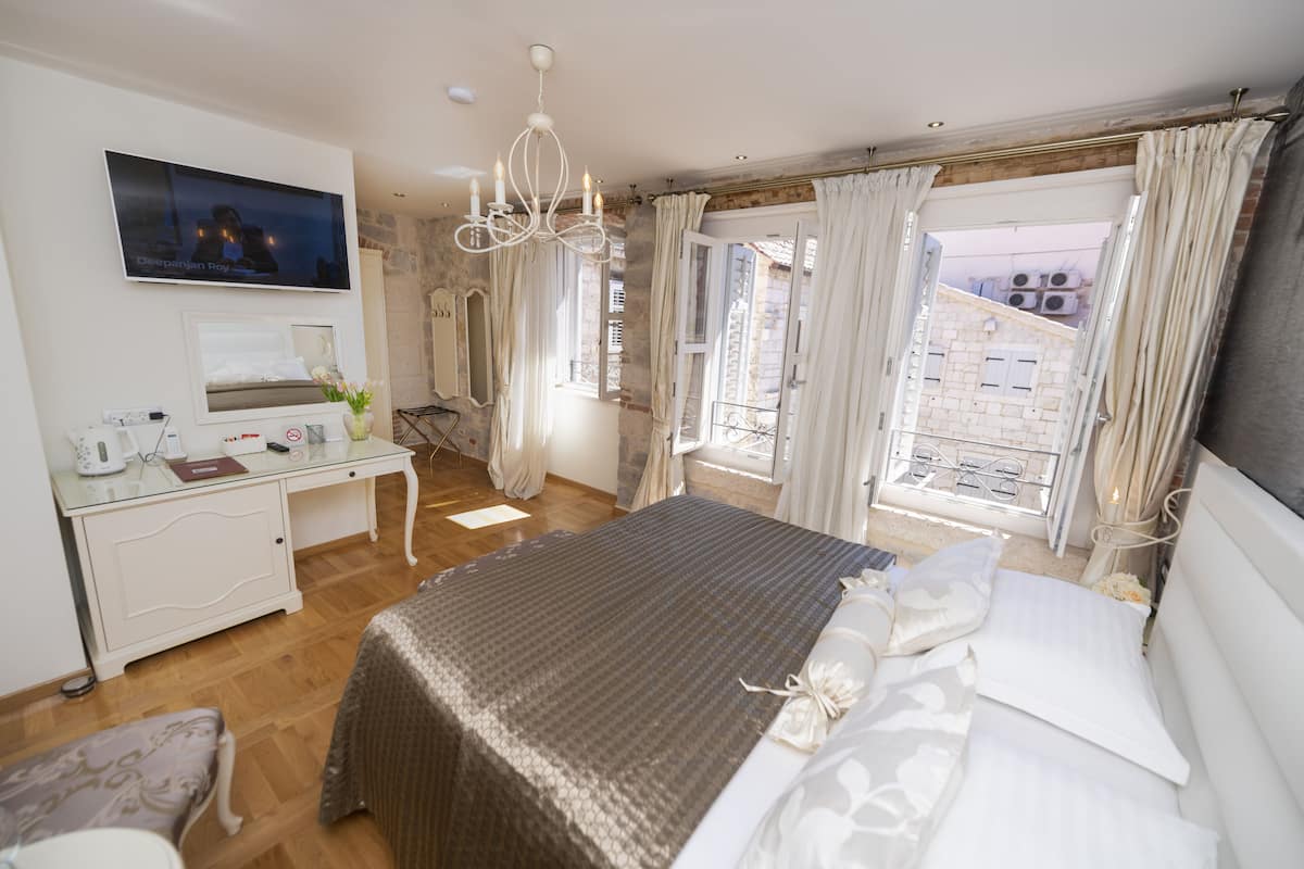 A bedroom with a bed, a desk, a TV, and a view of the outside.