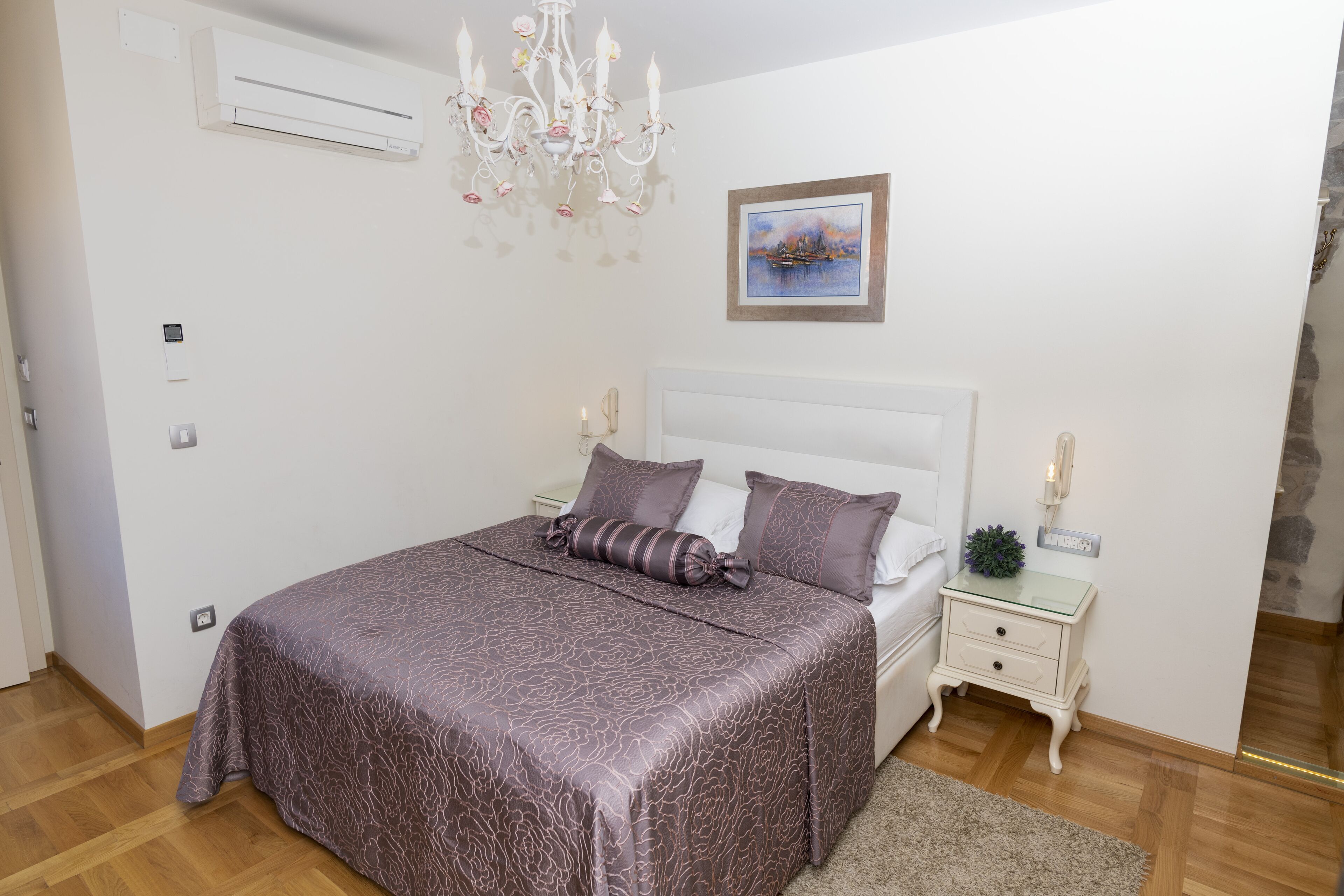 Ein Schlafzimmer mit einem großen Bett, einer Chandelier, einem Bild an der Wand und einem kleinen Nachttisch mit einer Lampe.