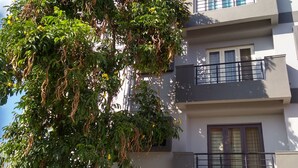 A multi-story residential building with balconies, a tree with hanging vines, and a parked car in the driveway.